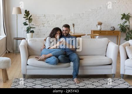 Happy millennial husband and wife using smartphone together at home Stock Photo