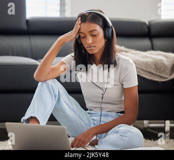 I dont understand how this works. an attractive young woman wearing headphones and feeling stressed while using her laptop. Stock Photo