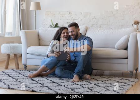 Happy laughing married couple using tablet, sharing digital device Stock Photo