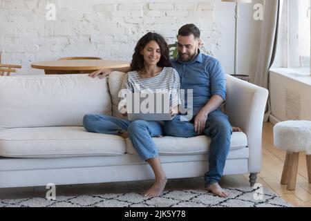 Happy engaged millennial couple in love sitting on couch Stock Photo