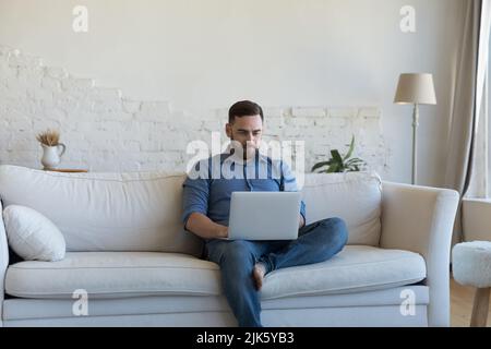Focused freelancer man using laptop, holding computer on lap Stock Photo