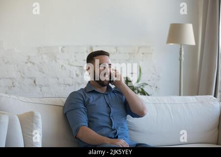 Cheerful millennial man talking on mobile phone at home Stock Photo