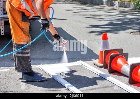 A road worker paints a white road marking of a pedestrian crossing with an airbrush on a sunny day. Stock Photo