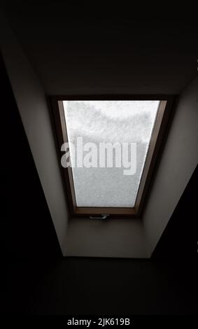 Roof window covered with snow. The snow on the glass blocks the light in a dark room. Stock Photo