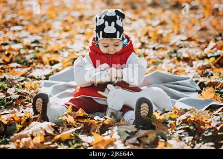 Little cute girl drinks tea from a thermos in the autumn park. Cute little toddler baby with thermos and cup Stock Photo