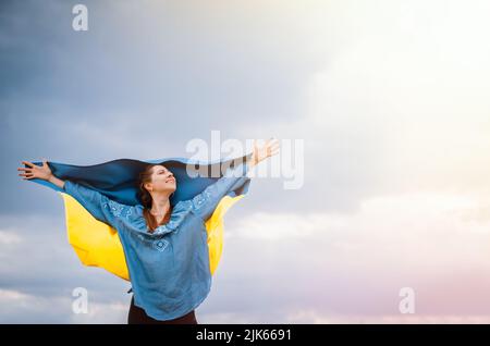 Happy free ukrainian woman with national flag on dramatic sky background. Portrait of lady in blue embroidery vyshyvanka shirt. Copy space. Ukraine Stock Photo