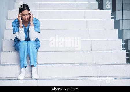 Our frontline workers are under so much pressure. a female nurse looking stressed while sitting on a staircase. Stock Photo