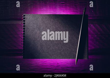 Black paper notebook on black wooden planks in purple neon light Stock Photo