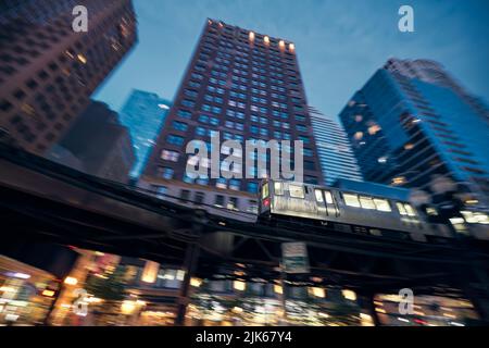 Elevated train in Chicago in blurred motion against skyscrapers in downtown disctrict at night. Stock Photo