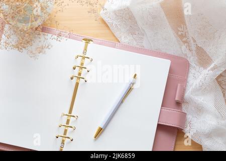 Flat lay, top view of a pastel pink planner, dried flower bouquet and stationery on a wooden desk. Stock Photo