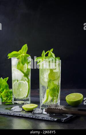 Mojito cocktail, mint, lime slices and ice cubes on a dark background. Cocktail mojito, ice tongs and cocktail spoon on slate board. Copy space Stock Photo