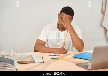 Tired dressmaker working with drawings and laptop Stock Photo