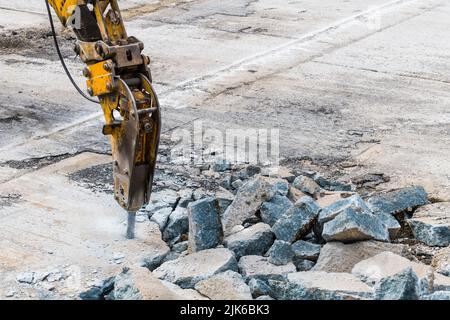 Excavator mounted hydraulic jackhammer at breaking a concrete area. Closeup of working demolition hammer. Heavy equipment detail on construction site. Stock Photo