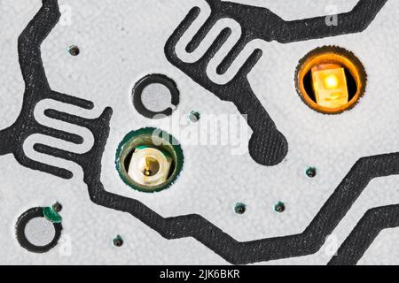 Lit and non-lit LED diode in small holes of PCB detail from dismantled cellphone. Close-up of electronic light emitting sources for buttons backlight. Stock Photo