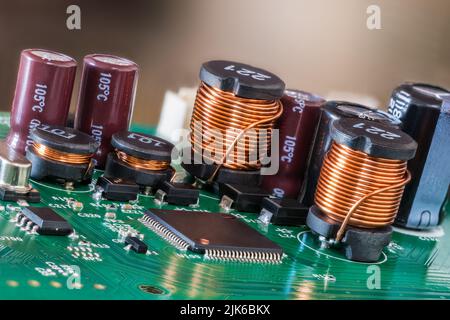 Closeup of electromagnetic coils and electrolytic capacitors or chips on green PCB. Various electrical components on printed circuit board. Inductors. Stock Photo