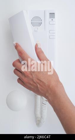 Close-up of a woman's hand opens a home front door using an intercom,intercom in the apartment,security phone.White intercom on the background of a wh Stock Photo