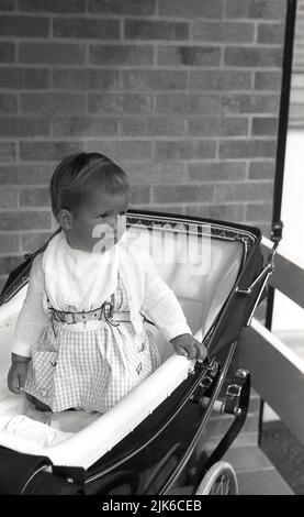 1960s, historical, strapped in with a harness, a soulful looking infant ...