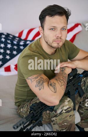 Soldier waiting on couch with his gun near American flag Stock Photo