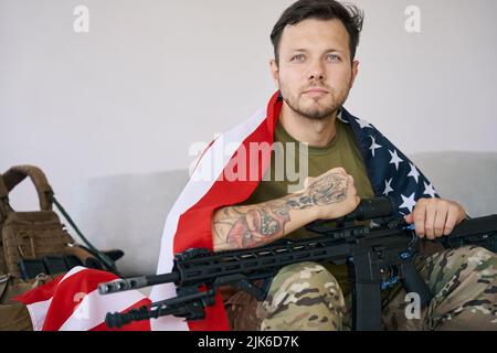 Confident soldier with American flag and rifle on couch Stock Photo