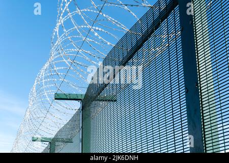 The image shows razor wire barbed tape coiled along the top of a metal fence. The wire is a secure deterrent and provides security for the premises Stock Photo