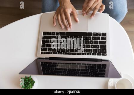 Young woman using laptop, sitting at coffee table, typing Stock Photo