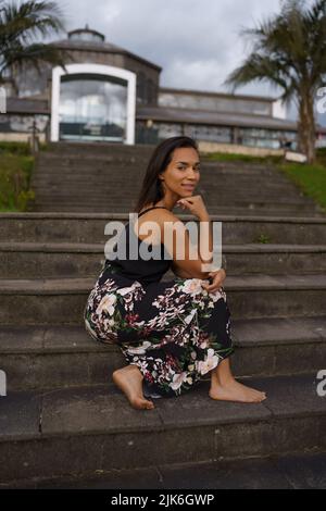 female model sitting on a bleachers, beautiful brunette latin woman with short black hair, lifestyle and beauty in the city Stock Photo
