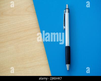 Silver ballpoint pen on blue and wooden background with copy space, top view. Flat lay of a metallic, steel, metal pen. Stock Photo