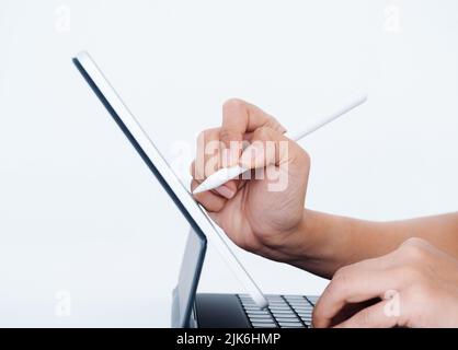 Hand holding white electronic pen or pencil, writing or drawing on digital tablet screen while typing on keyboard computer isolated on white backgroun Stock Photo