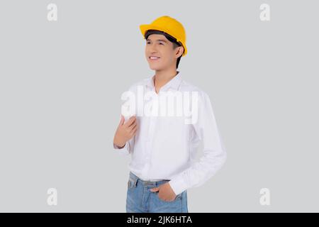 Portrait young asian man is engineer wearing helmet standing and holding blueprint with confident isolated on white background, handsome male is archi Stock Photo