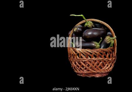 Image of a wicker basket with an eggplant harvest on a black background Stock Photo