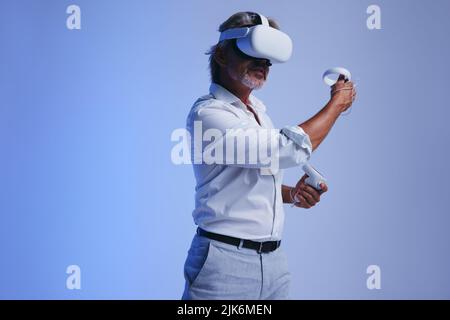Senior businessman giving a presentation in virtual reality. Mature businessman using a pair of gaming controllers to conduct a meeting in cyberspace. Stock Photo