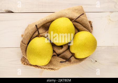 Three sweet bright yellow pears with a jute bag on a wooden table, close-up, top view. Stock Photo