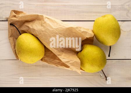 Three sweet bright yellow pears with a paper craft bag on a wooden table, close-up, top view. Stock Photo