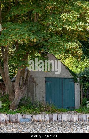 beach hut under trees on the beach, boathouse with blue wooden doors under the shade of some trees on a beach, old fashioned rustic boathouse Stock Photo
