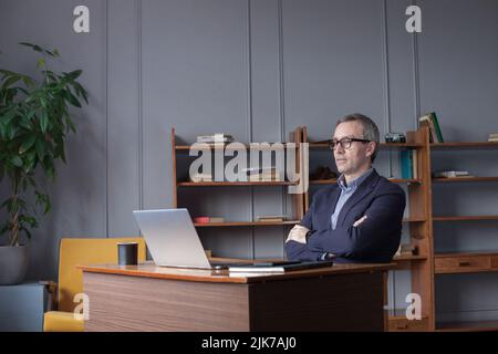 Professional man sitting in office in front of laptop. Developer thinking on solutions for work. Home-based worker on desktop. Stock Photo