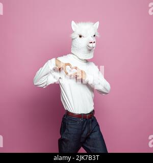 Man wearing lama mask making heart with hands on bright pink background Stock Photo