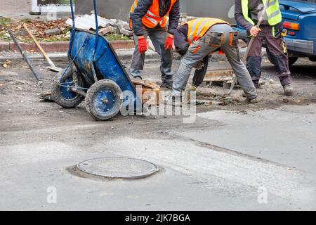 A team of road workers are replacing a sewer manhole on a carriageway on a summer day. Copy space. Stock Photo