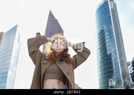 Happy teen redhead girl standing on big city urban street looking at camera. Stock Photo