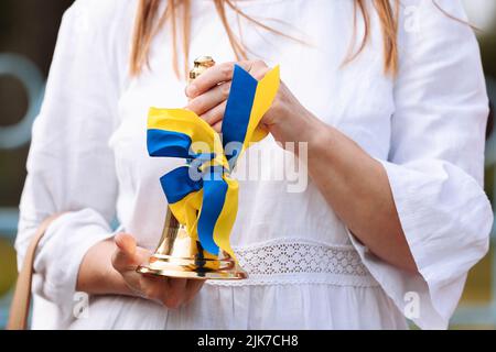 cropped photo of female hands holding school bell with a blue yellow bow - a symbol of the beginning of the school year or graduation in Ukraine. Conc Stock Photo