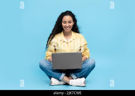 Arabic Lady Working Online On Laptop Sitting Over Blue Background Stock Photo