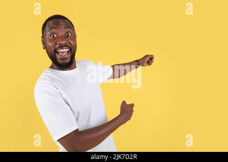 Excited Black Man Pointing Fingers Aside Over Yellow Studio Background Stock Photo