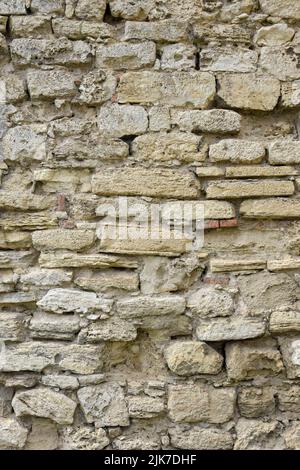 Masonry wall of old stone blocks of limestone. Background texture of ancient brick wall. Full frame. Vertical photo. Selective focus. Stock Photo