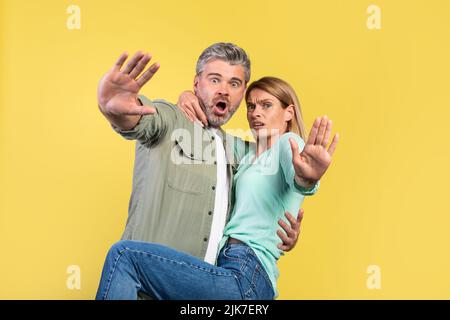 Omg. Portrait of scared middle aged spouses screaming and gesturing stop, woman jumping on husband, looking at camera Stock Photo