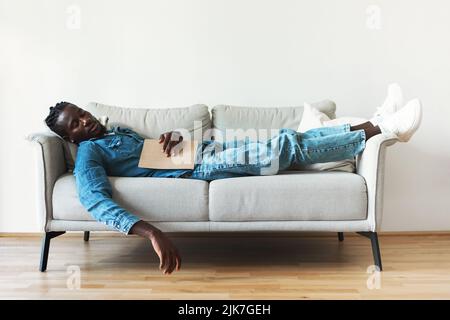 African Guy Sleeping Holding Book Resting Lying On Couch Indoor Stock Photo
