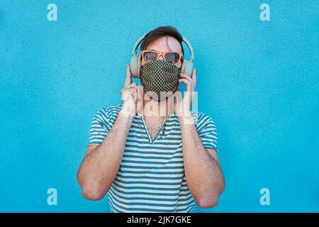 Young man listening music with big headphones and face mask on in coronavirus time  - Boy in summer bright background feeling cheerful in social dista Stock Photo