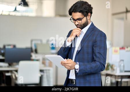 Busy indian young business man executive wearing suit using digital tablet. Stock Photo