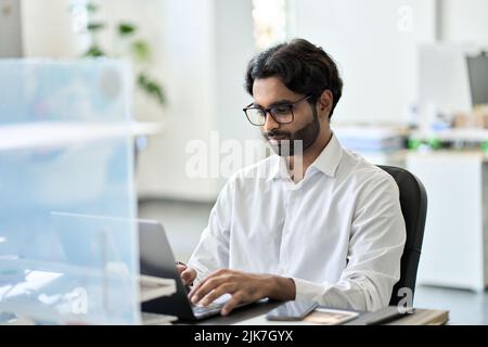 Young busy indian business man office worker working on laptop sitting at desk. Stock Photo