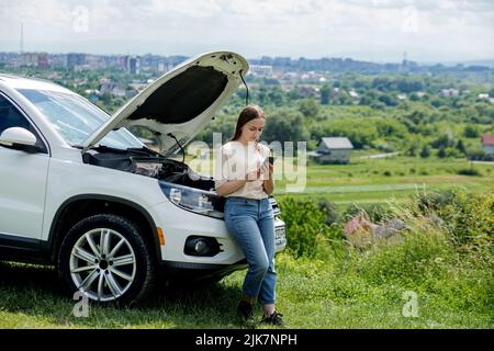 Young woman opening bonnet of broken down car having trouble with her vehicle. Worried woman talking on the phone near broken car Stock Photo