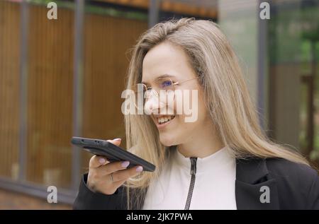 Happy girl records an audio message on a smartphone. Calls on the speaker, gives a command to a virtual assistant, uses a voice recognition applicatio Stock Photo