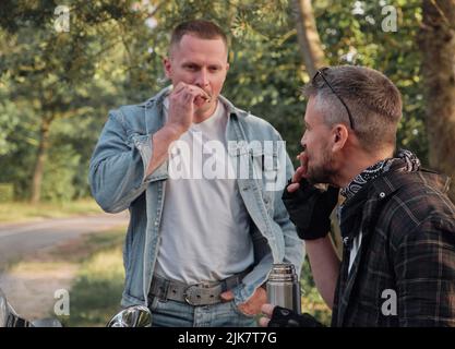 Two man friends of motorcyclists bikers on motorcycles smoking on the side of the road and talking Stock Photo